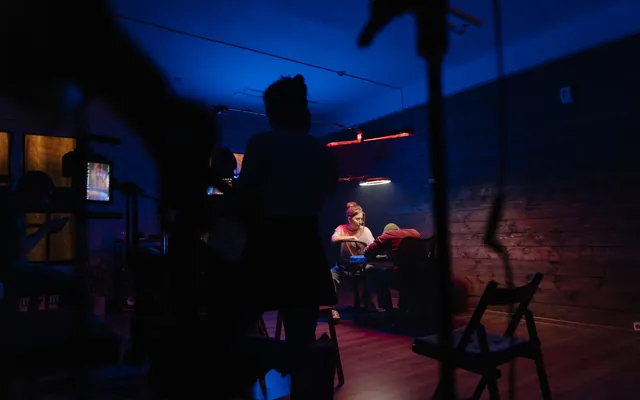 A production crew filming a scene on a neon-lit studio set.