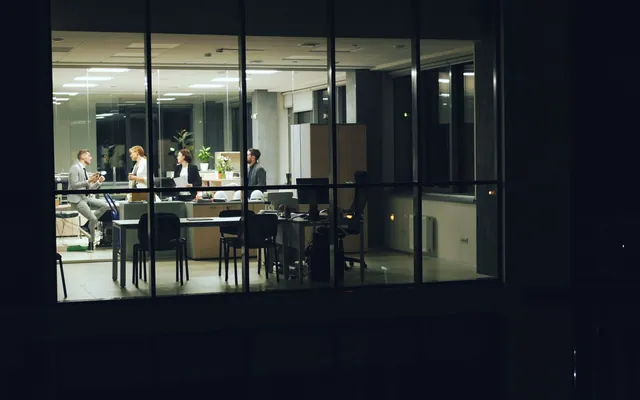 A team working late around a table in a glass-walled office at night.